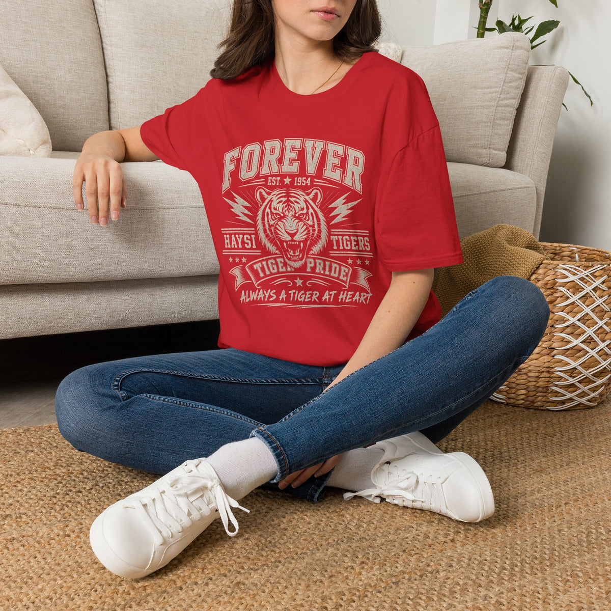 A woman wearing a bright red graphic t-shirt. The shirt features a white distressed print of a tiger head and the text 'FOREVER HAYSI TIGERS EST 1954 TIGRE PRIDE ALWAYS A TIGER AT HEART'.