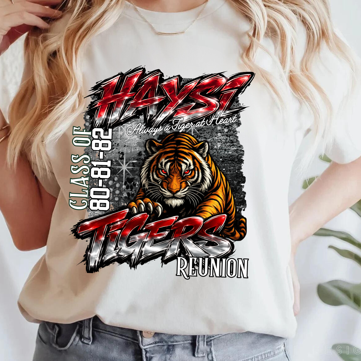 A woman wearing a white graphic t-shirt featuring a tiger and the text 'HAYST TIGERS Class of 80-82 Reunion'.