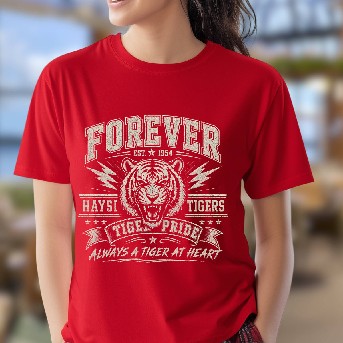 A  bright red short-sleeve t-shirt with a vintage-style white graphic print featuring a tiger, the text 'FOREVER EST. 1954', 'HAYSI TIGERS', and 'ALWAYS A TIGER AT HEART'.