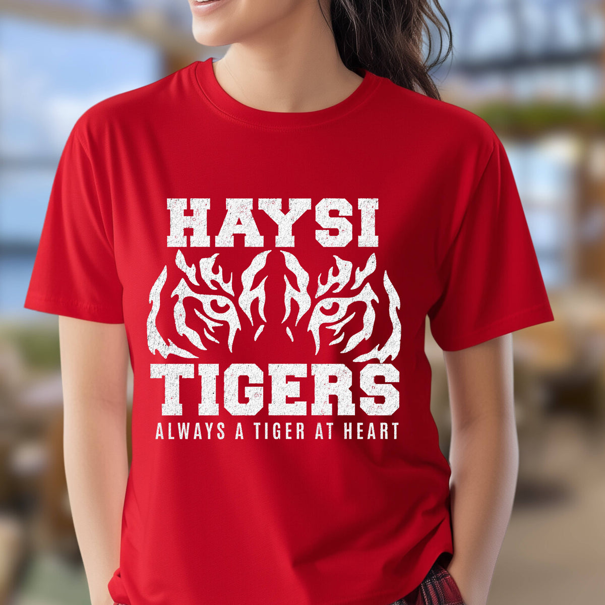 A woman wearing a bright red short-sleeve t-shirt with a distressed white graphic that reads 'HAYSI TIGERS ALWAYS A TIGER AT HEART' with a tiger face.
