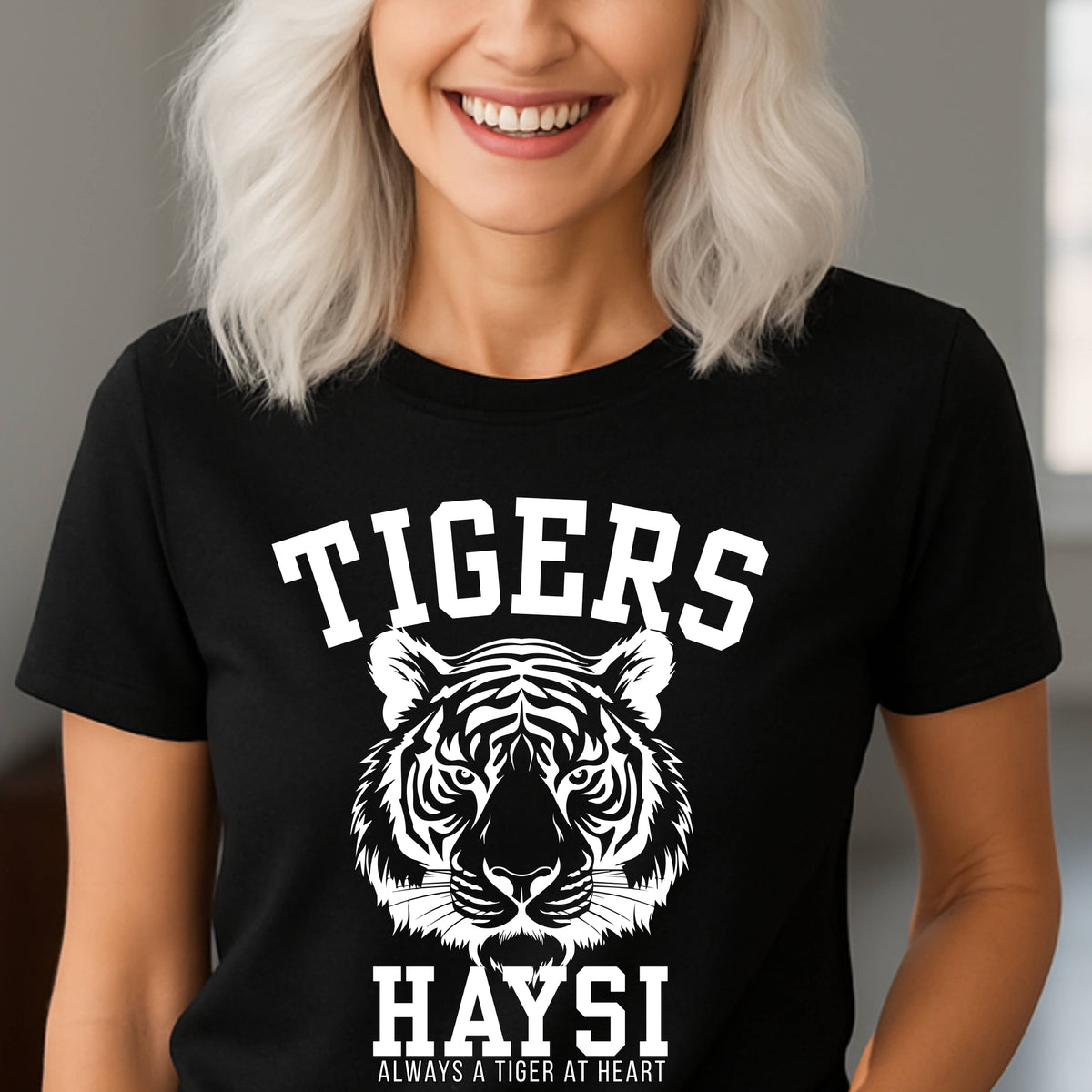 A woman with white hair wearing a black short-sleeve t-shirt with a white graphic print of a tiger head and the text 'TIGERS HAYSI ALWAYS A TIGER AT HEART'.
