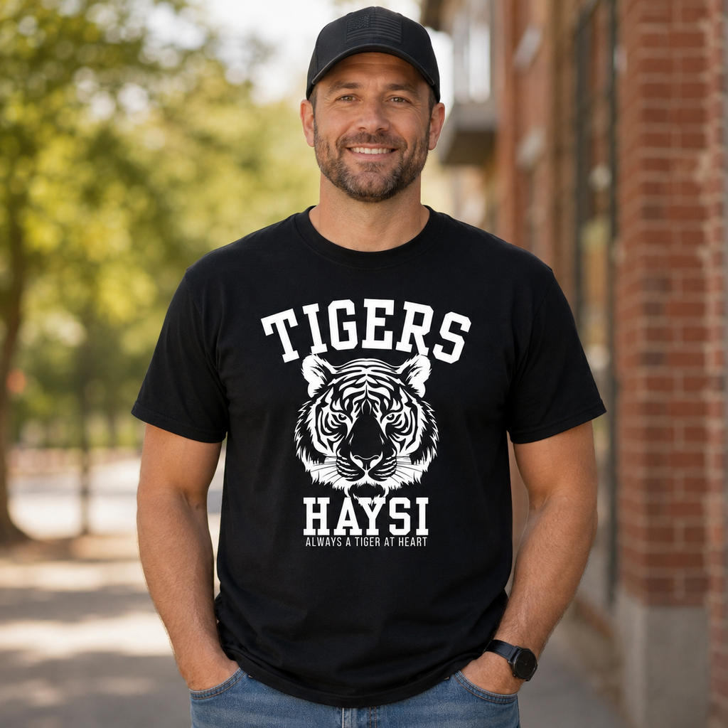 A man wearing a black crewneck t-shirt with a white graphic of a tiger head and the text 'TIGERS HAYSI ALWAYS A TIGER AT HEART', standing outdoors in front of a brick building.