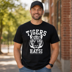 A man wearing a black crewneck t-shirt with a white graphic of a tiger head and the text 'TIGERS HAYSI ALWAYS A TIGER AT HEART', standing outdoors in front of a brick building.