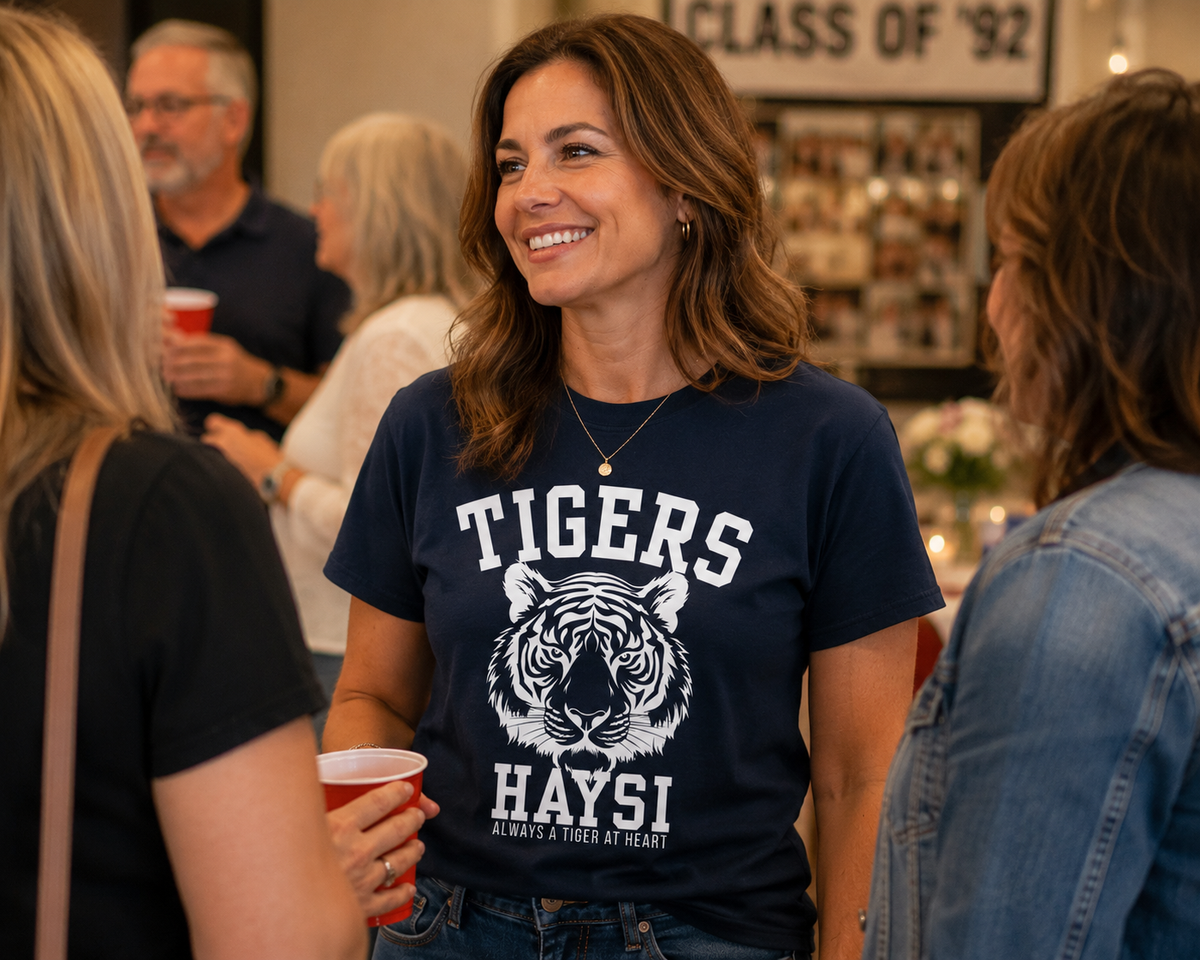 A woman smiling in a social setting, wearing a navy blue graphic t-shirt with a white tiger illustration and the text 'TIGERS HAYSI'.