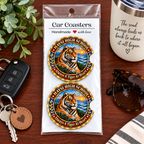 Two round car coasters featuring a tiger illustration and the text 'HAYS! HIGH SCHOOL' and 'Always A Tiger At Heart,' packaged in a clear plastic sleeve on a wooden tabletop with a key fob, mug, sunglasses, and greenery nearby.
